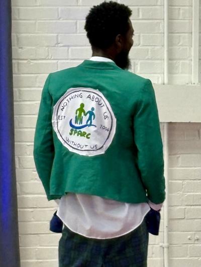 A SPARC participant models a green blazer hand-painted with the SPARC seal and the motto "Nothing About Us Without Us" at the inclusive fashion show